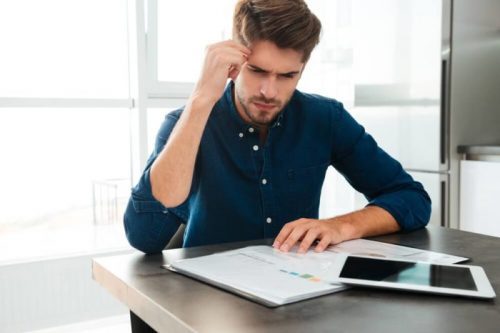 graphicstock-photography-of-concentrated-young-man-sitting-at-home-and-analyzing-his-finances-looking-at-documents-and-touching-his-head_S_-oiKhB3e